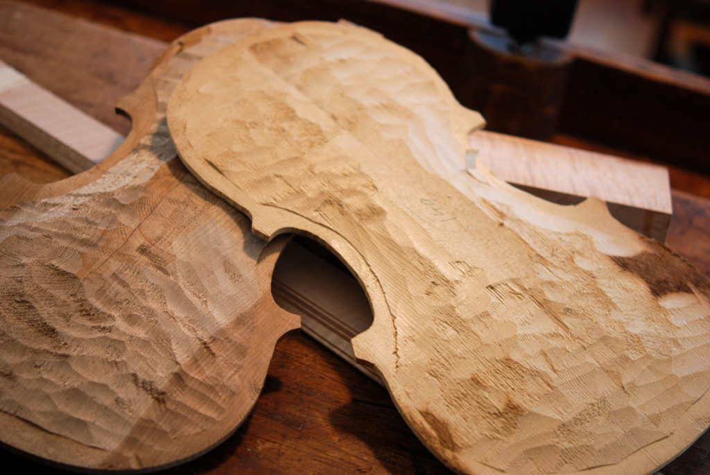 Two carved wooden violin tops and blocks of wood on a workbench